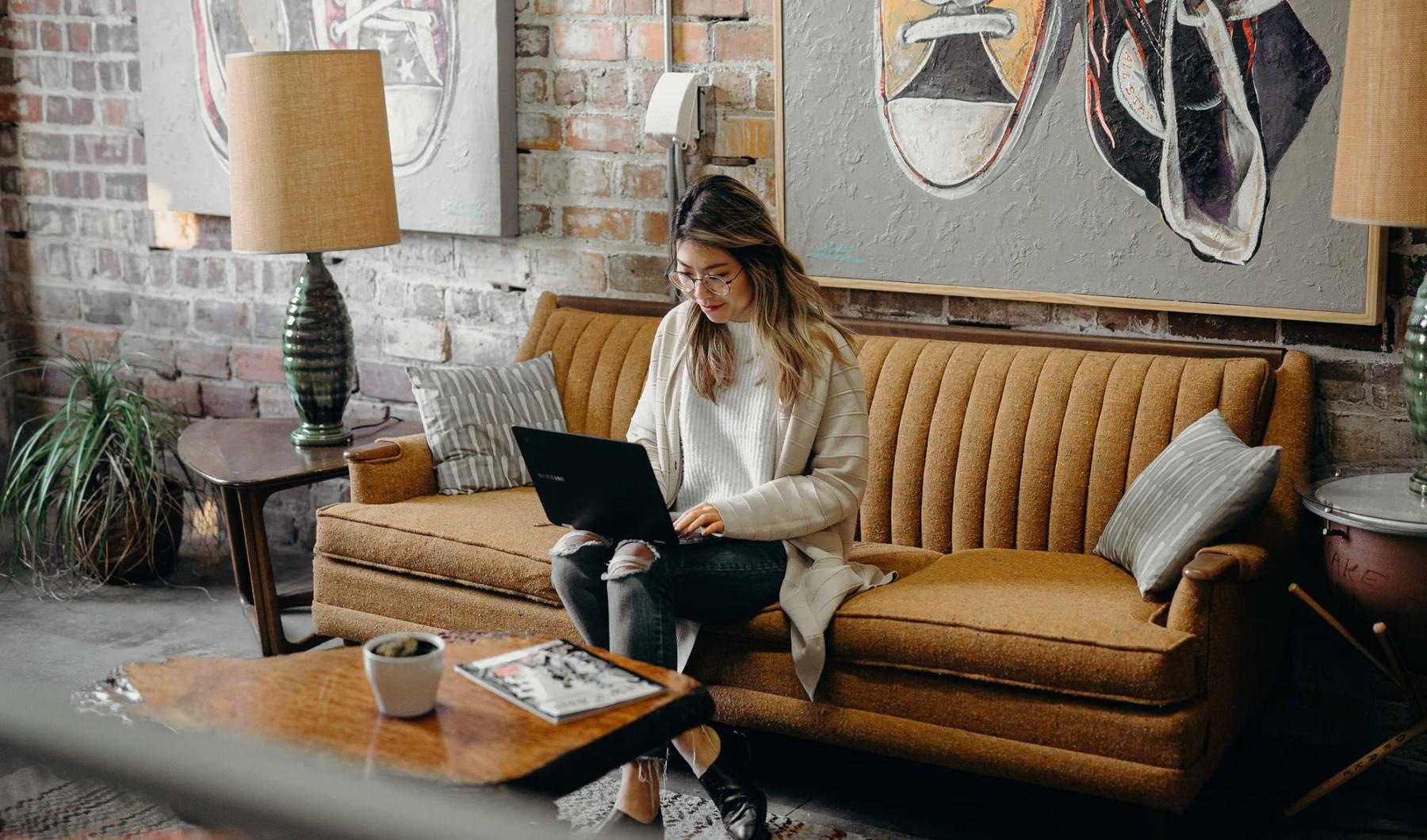 a woman sitting on a couch working on a laptop